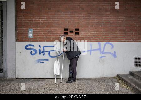 Un anziano si trova contro un muro mentre si riposa dal camminare su stampelle, fumare una sigaretta, Braunschweig, Germania Foto Stock