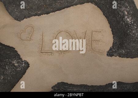 Iscrizione con testo d'amore e forma del cuore disegnati nella sabbia e incorniciati da rocce nere Foto Stock