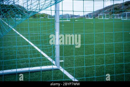 Linee intorno al campo da calcio, lato angolo, in prato sintetico. Vista dietro la rete sul campo di calcio sulle isole Lofoten circondato da rocce Foto Stock