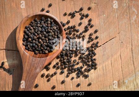 Grani di pepe nero in cucchiaio di legno su fondo di legno Foto Stock