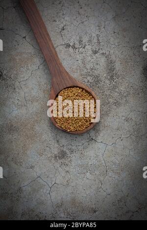 Semi di fenugreek in cucchiaio di legno su fondo di struttura di calcestruzzo fessurato Foto Stock