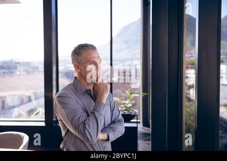 Uomo d'affari caucasico che pensa accanto a una finestra Foto Stock