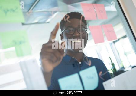 Uomo afro-americano che scrive su un bordo trasparente in un ufficio Foto Stock