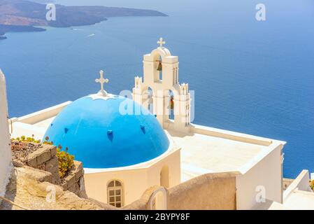 La Chiesa Cattolica della Vergine Maria a cupola blu e le tre campane di Fira sull'isola greca di Santorini, che si affaccia sulla caldera e sul mare Egeo Foto Stock