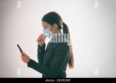 COVID-19 applicazione di tracciamento dei contatti sul telefono cellulare donna che cammina all'esterno mentre si indossa una maschera medica chirurgica a contatto con il viso testando smartphone Foto Stock