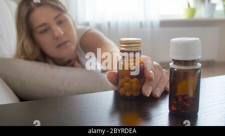 Immagine closeup di giovane donna malata che raggiunge per pillole sul comodino Foto Stock