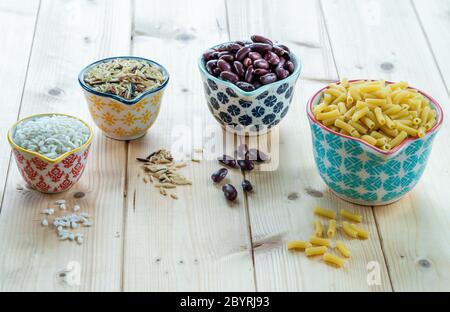 Riso secco, fagioli e pasta in pentole di ceramica su fondo di legno Foto Stock