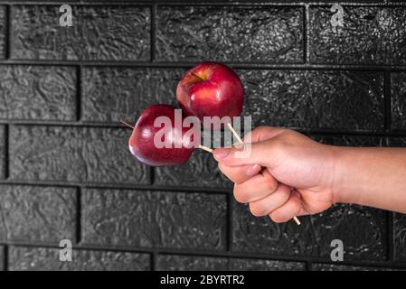 Mano dell'uomo che tiene le mele rosse con i bastoni di legno su uno sfondo nero Foto Stock