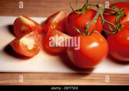 Pomodoro in quattro pezzi con mazzo di pomodori interi su cibo bianco da tagliere Foto Stock