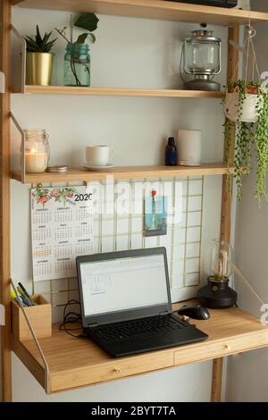Piccola stazione remota per ufficio domestico, con computer portatile, piante domestiche, lavagna metallica, candele e lampada da tavolo. Shot verticale. Foto Stock