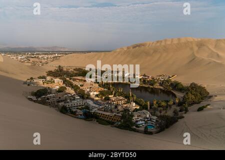 oasi nel mezzo del deserto, con molti alberi ed edifici, nuvole e cielo blu Foto Stock