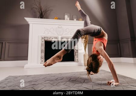 Giovane ragazza molto flessibile che fa yoga nella stanza del minimalismo Foto Stock