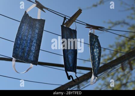 Maschere facciali fatte in casa da una tela dopo il lavaggio per asciugare su una stendibiancheria retroilluminata contro un cielo blu, protezione contro le infezioni durante il decor Foto Stock