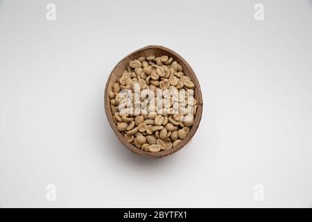 Primo piano di chicchi di caffè crudo in una ciotola con guscio di cocco isolata su sfondo bianco con spazio per la copia Foto Stock