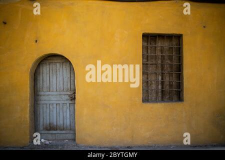 L'esterno di un vecchio negozio giallo con una porta blu chiusa a chiave e una finestra di legno intemperie con una recinzione di ferro arrugginita, Istanbul, Turchia Foto Stock