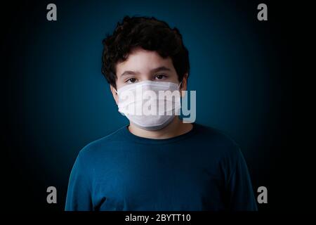 ragazzo bianco che guarda la fotocamera indossando una maschera di protezione respiratoria su sfondo scuro Foto Stock