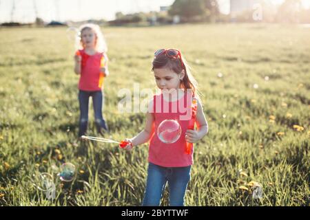 Prendere una bolla. Ragazze amici che soffiano bolle di sapone nel parco il giorno d'estate. I bambini si divertono all'aperto. Autentico momento magico dell'infanzia felice. Stile di vita s Foto Stock