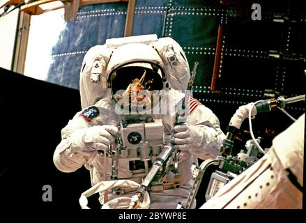 (13 febbraio 1997) --- l'astronauta Steven L. Smith raccoglie un utensile a cricchetto di potenza mentre si prepara ad unirsi all'astronauta Mark C. Lee (fuori dal telaio) sulla prima passeggiata spaziale della missione STS-82 per servire il telescopio spaziale Hubble (HST), temporaneamente bloccato nella baia del carico di Discovery?s (sfondo) Foto Stock