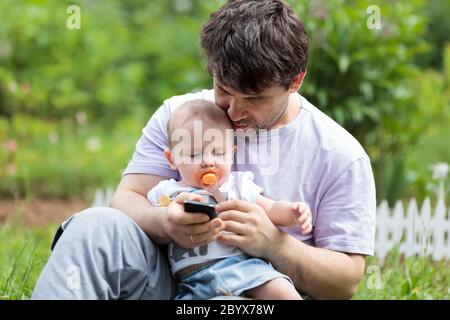 Padre tenendo un bambino e gli sms sul suo cellulare Foto Stock