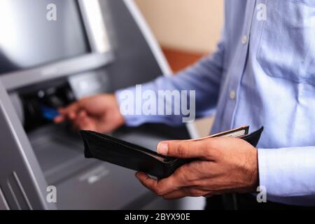 Uomo con un portafoglio nero aperto presso ATM Machine, inserendo una carta di credito. Transazione ATM. Primo piano. Messa a fuoco morbida. Terminale POS. Foto Stock