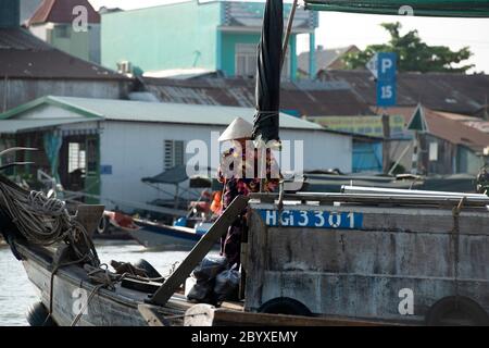 Una donna usa il suo telefono mentre indossa un cappello conico vietnamita (non la) sulla sua barca sul fiume Hau a Can Tho, regione del delta del Mekong, Vietnam meridionale. Foto Stock
