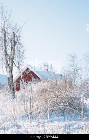 Tipico scenario invernale svedese, antico casale rosso nella neve, sole e cielo blu Foto Stock