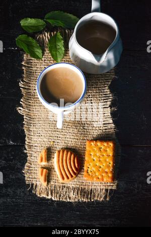 Una tazza di tè con gustosi biscotti, teiera e foglie fresche su vecchio sfondo scuro di legno Foto Stock