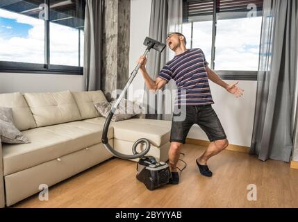 L'uomo cantava nel soggiorno di casa sua tenendo l'aspirapolvere come se fosse un microfono. Corpo intero. Foto Stock