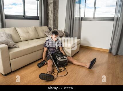 Uomo seduto sul pavimento nel soggiorno cercando di capire come funziona un aspirapolvere. Corpo intero. Foto Stock