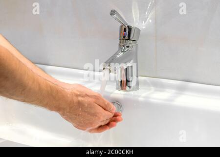 Primo piano di un giovane uomo caucasico che si lava le mani con sapone nel lavello del bagno igiene personale, protezione contro virus e batteri concetto Foto Stock