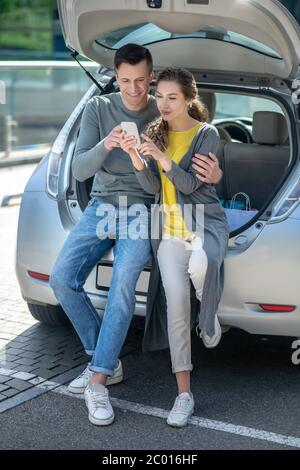 Un giovane uomo e una donna con smartphone riposano vicino all'auto Foto Stock