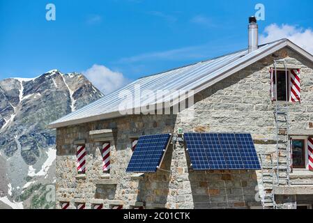 Immagine orizzontale della capanna alpina che si trova nelle Alpi Pennine, pannelli solari installati sulle pareti come fonte alternativa di energia, concetto di energia sostenibile Foto Stock