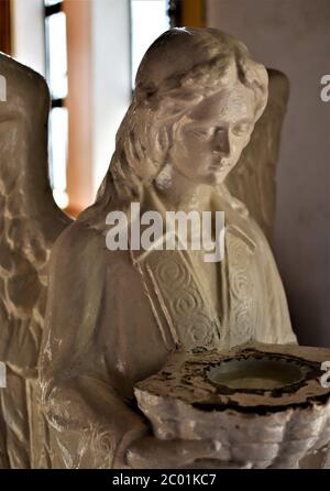 Una statua di un angelo all'ingresso di una chiesa che tiene un bacino che serve come una stoup per l'acqua Santa Foto Stock