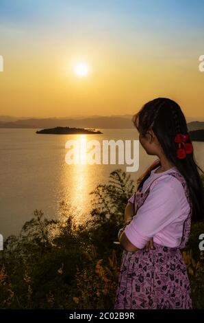Felice giovane donna che guarda il tramonto sul lago Foto Stock