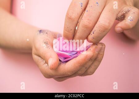 Mani per bambini con glitter e confetti di colore blu e argento su sfondo rosa pastello. Foto Stock