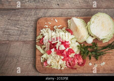 Verdure biologiche fresche, cavolo e pomodori tritati, verdi, aneto, prezzemolo su tavola di legno e un tavolo rustico, posto per un'iscrizione Foto Stock