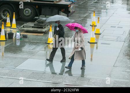 WESTMINSTER LONDON, REGNO UNITO. 11 giugno 2020. Pedoni che indossano maschere di protezione al riparo sotto un ombrello in Trafalgar Square in una giornata piovosa a Londra . Credit: amer Ghazzal/Alamy Live News Foto Stock