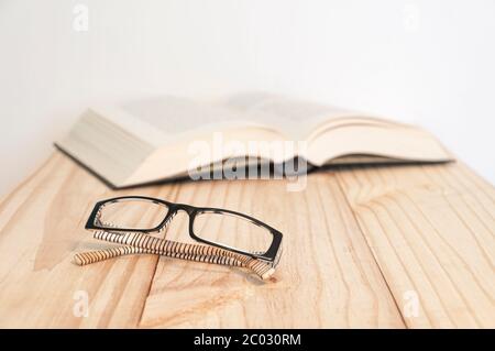In primo piano un paio di vetri bianchi e neri, lo sfondo (fuori fuoco) un libro su un tavolo di legno Foto Stock