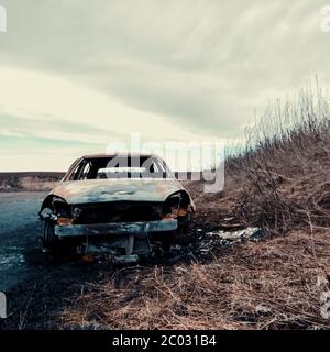 Auto abbandonata sul lato della strada con erba, pozzanghere e cielo - 'fine della strada' Foto Stock