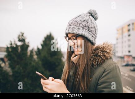 Vista laterale della ragazza millenaria che chattava online sul cellulare Foto Stock