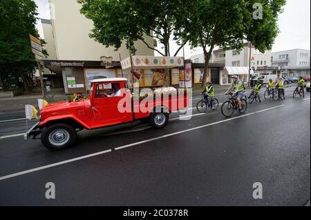 Colonia, Germania. 11 Giugno 2020. Un vecchio camion pick-up della vigna del fuoco, accompagnato da alacari ragazzi in bicicletta, trasporta la mostruosità della comunità cattolica di Colonia-Porz attraverso le strade. Invece della tradizionale processione del Corpus Domini, dovuta alla pandemia di Corona, la mostruosità, il Santissimo Sacramento, è guidata dal Corpus Domini mobile verso dodici diverse stazioni, dove in ogni caso viene celebrato un breve servizio. Credit: Henning Kaiser/dpa/Alamy Live News Foto Stock