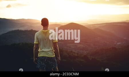 Giovane urlando sulla cima della montagna e godendo della totale libertà durante il tramonto. Escursionista rilassante in cima a una montagna e godere di vista sulla valle Foto Stock