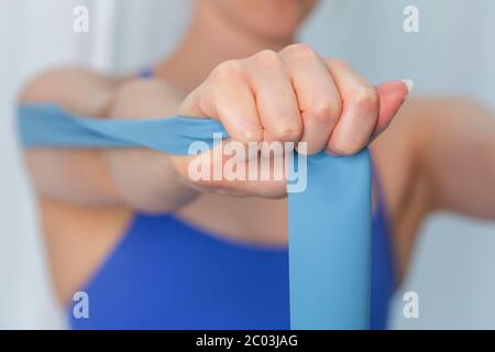 Giovane donna che si esercita a casa in top sport blu utilizzando una banda di resistenza Foto Stock