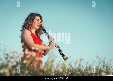 donna in un vestito rosso che gioca il clarinetto in un campo di margherite Foto Stock