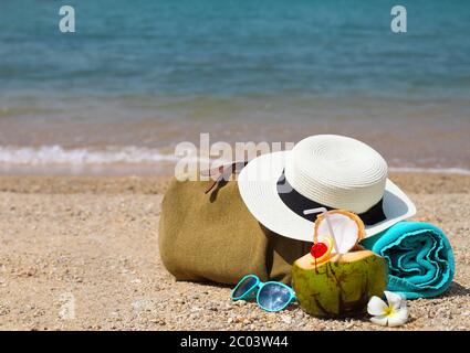Cappello di paglia, occhiali da sole, telo da spiaggia con borsa da mare e cocktail al cocco Foto Stock