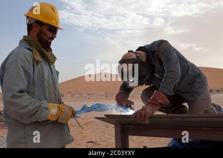 Saldatori in lavoro tagliano lamiera d'acciaio per la costruzione di un serbatoio di olio in un nuovo impianto petrolifero nel deserto del Sahara. Foto Stock