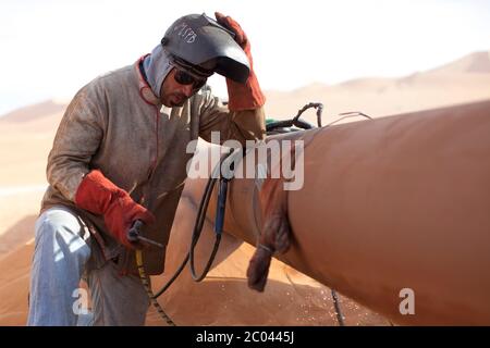 Un saldatore riposa un attimo mentre Welders si unisce a un oleodotto di esportazione nel deserto del Sahara per trasportare il petrolio dalle piattaforme di perforazione terrestri alla costa. Foto Stock
