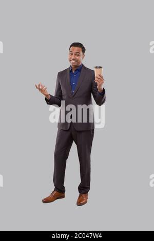 Businessman che tiene il caffè per andare tazza isolato. Uomo d'affari indiano con tazza di take away del caffè nelle mani Foto Stock