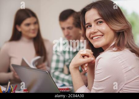 In prossimità di un grazioso felice giovane studentessa sorridente alla fotocamera sulla sua spalla, godendo di studiare con i suoi amici dell'università Foto Stock