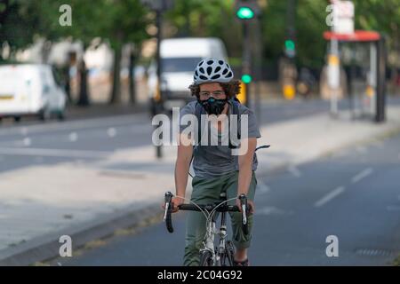 Giovane adulto che cavalca in biciletta in una pista ciclabile per pendolari lungo l'Embankment vicino al Tamigi nel centro di Londra, Inghilterra, indossando un mito facciale Foto Stock